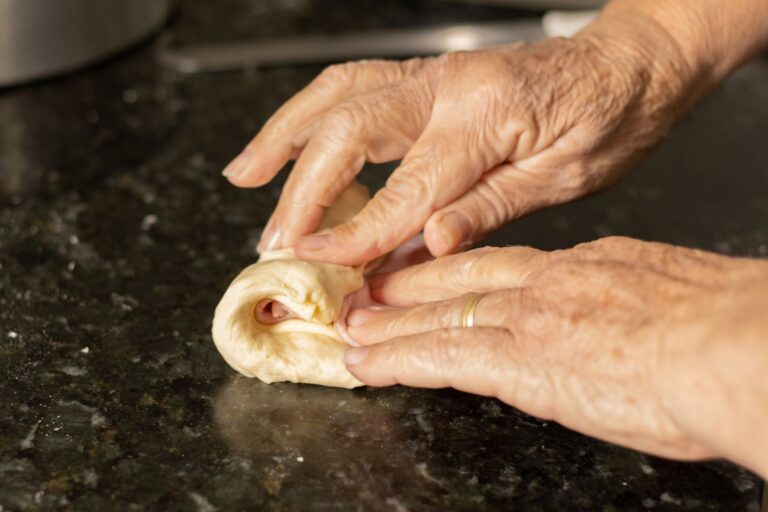 Mains étalant une pâte brisée au rouleau sur un plan de travail fariné